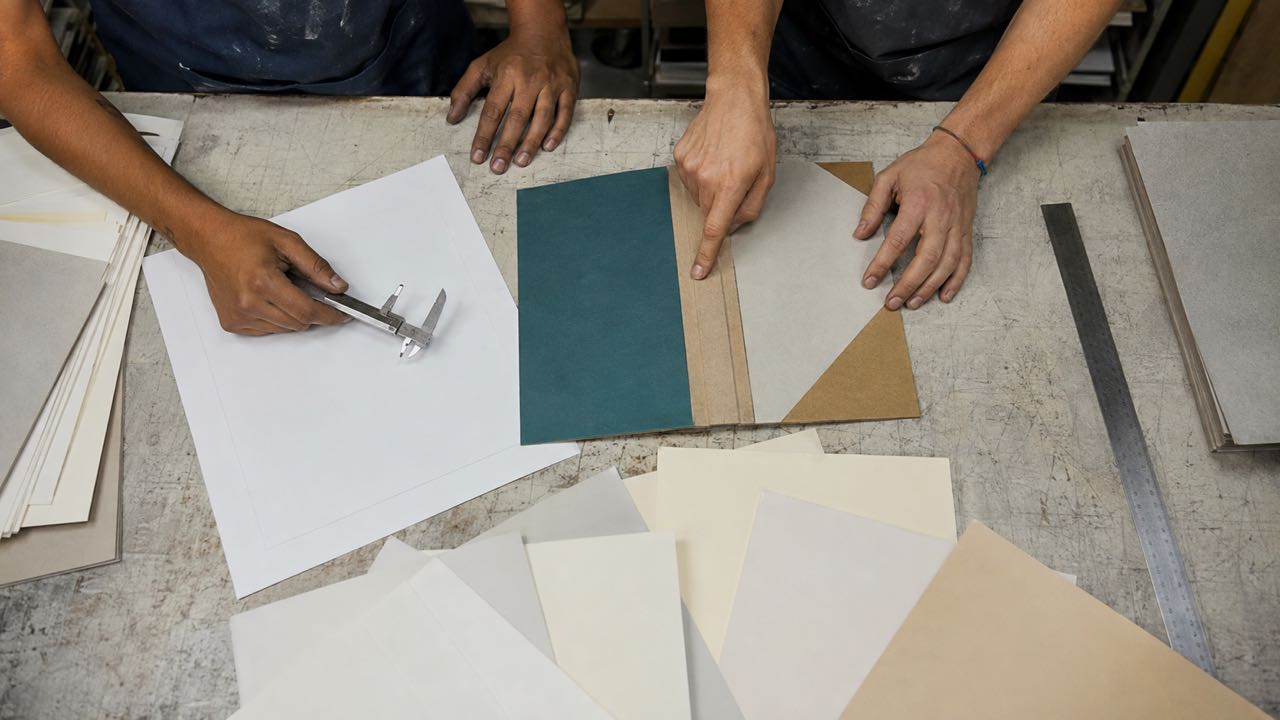 Muestras de papel, herramientas de medición y maqueta de cubierta sobre una ficha técnica